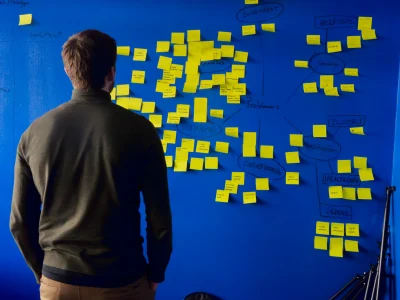 Man in a gray long-sleeved shirt standing in front of a blue wall with yellow post-its